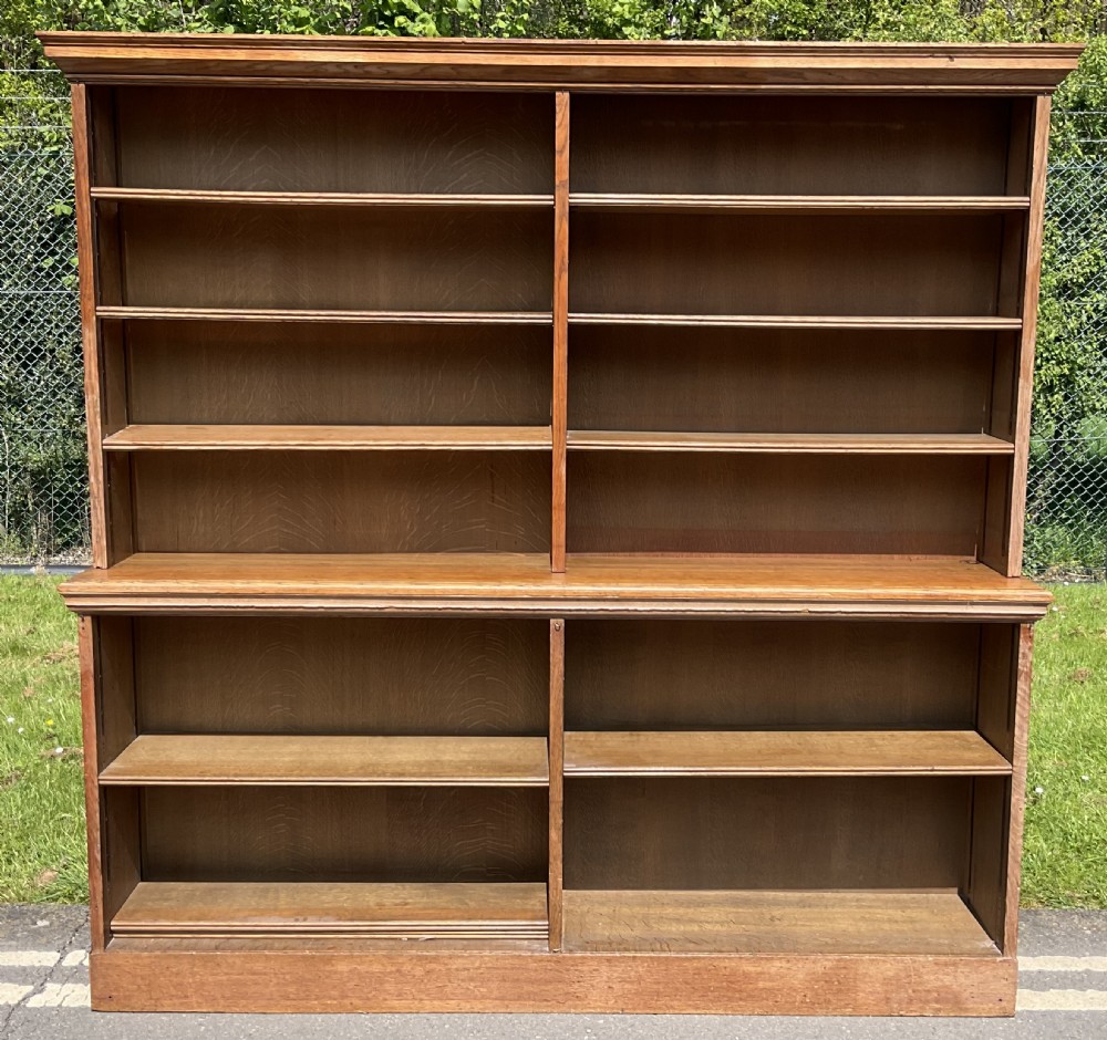 A large Edwardian open-front oak bookcase featuring two main sections with multiple horizontal shelves and a moulded cornice.