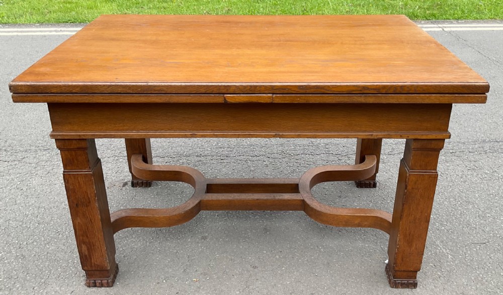 An Arts and Crafts style golden oak extending dining table featuring a rectangular draw-leaf top and a curved cross-stretcher base.