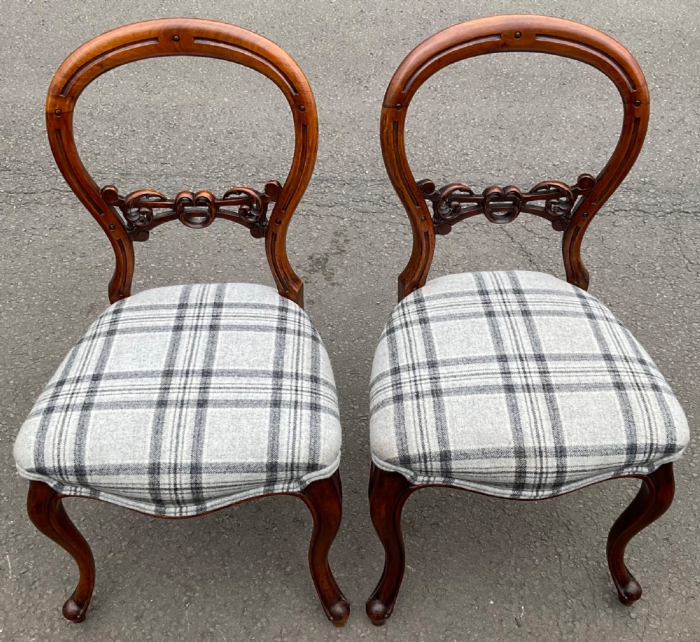A pair of Victorian walnut side chairs featuring balloon backs with carved central splats, cabriole legs, and grey tartan plaid wool seat cushions.