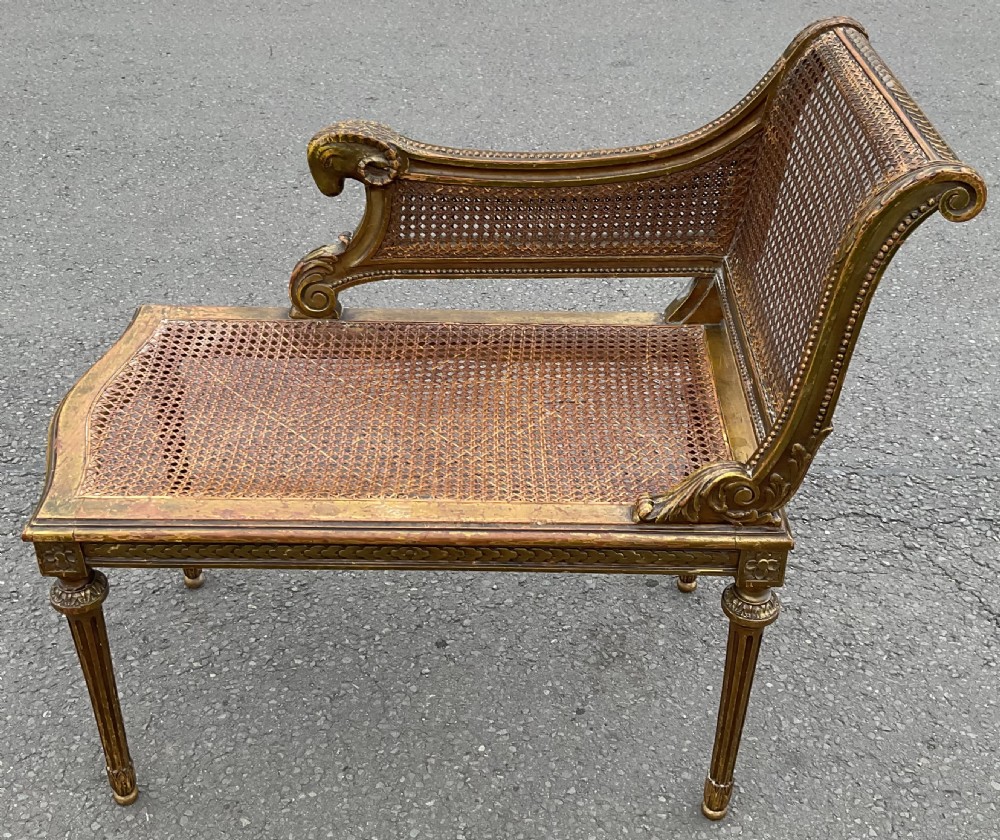 An antique French style caned window seat with a gilded wooden frame featuring carved ram head armrest terminals and tapered fluted legs.