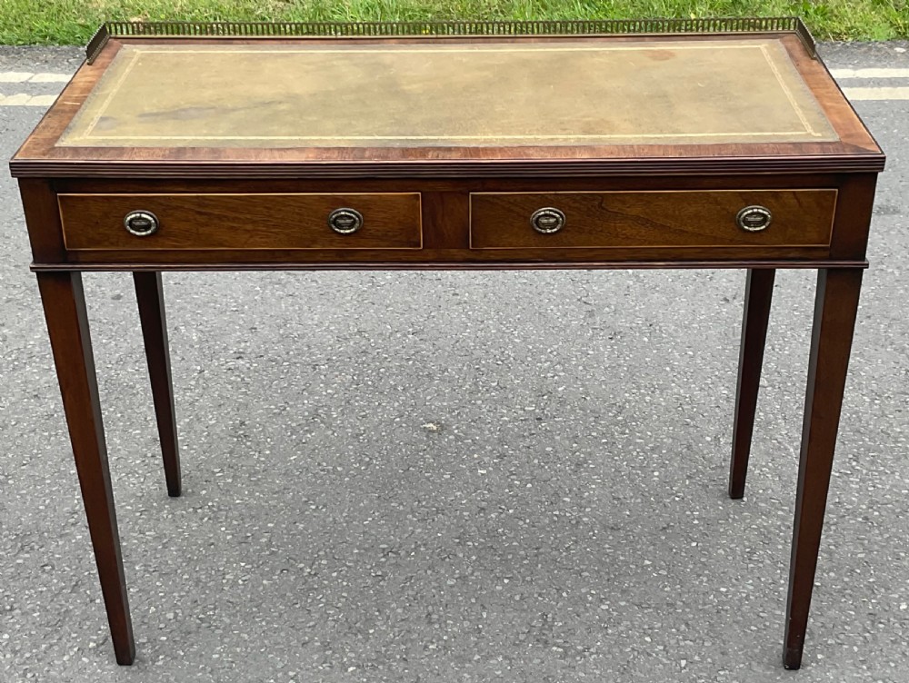 A Georgian style mahogany writing table featuring a leather insert top, brass gallery edge, two frieze drawers, and square tapered legs.