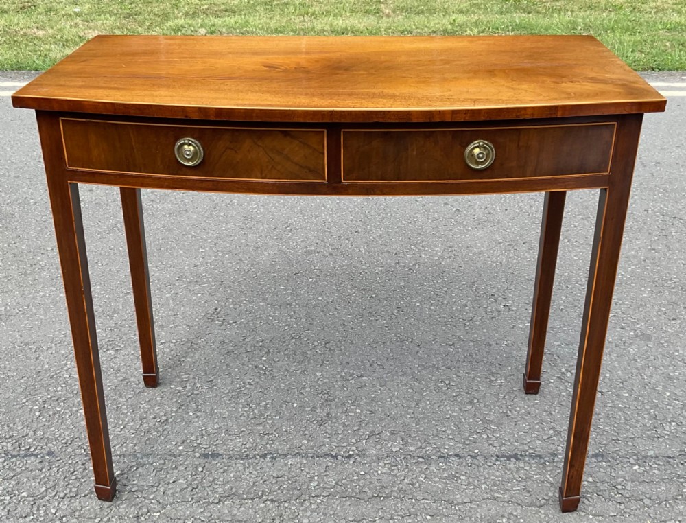 A Georgian bowfront mahogany side table featuring two drawers with brass ring handles and boxwood stringing inlay supported by square tapered legs.