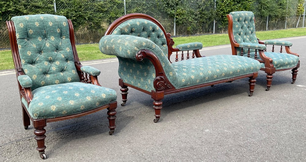 A Victorian carved mahogany chaise longue suite upholstered in patterned green fabric with button-tufted backs and turned legs on brass castors.