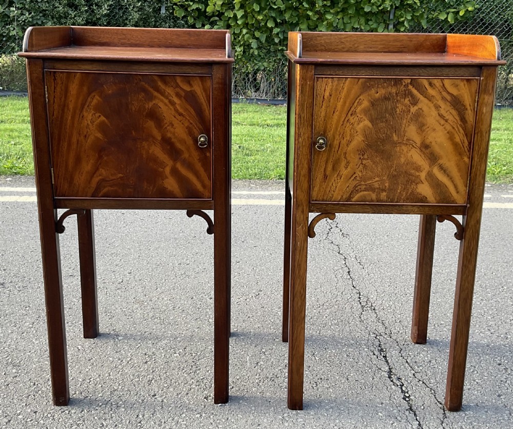 A pair of tall Edwardian mahogany bedside cabinets featuring gallery tops, flame mahogany single door fronts, and straight square legs.