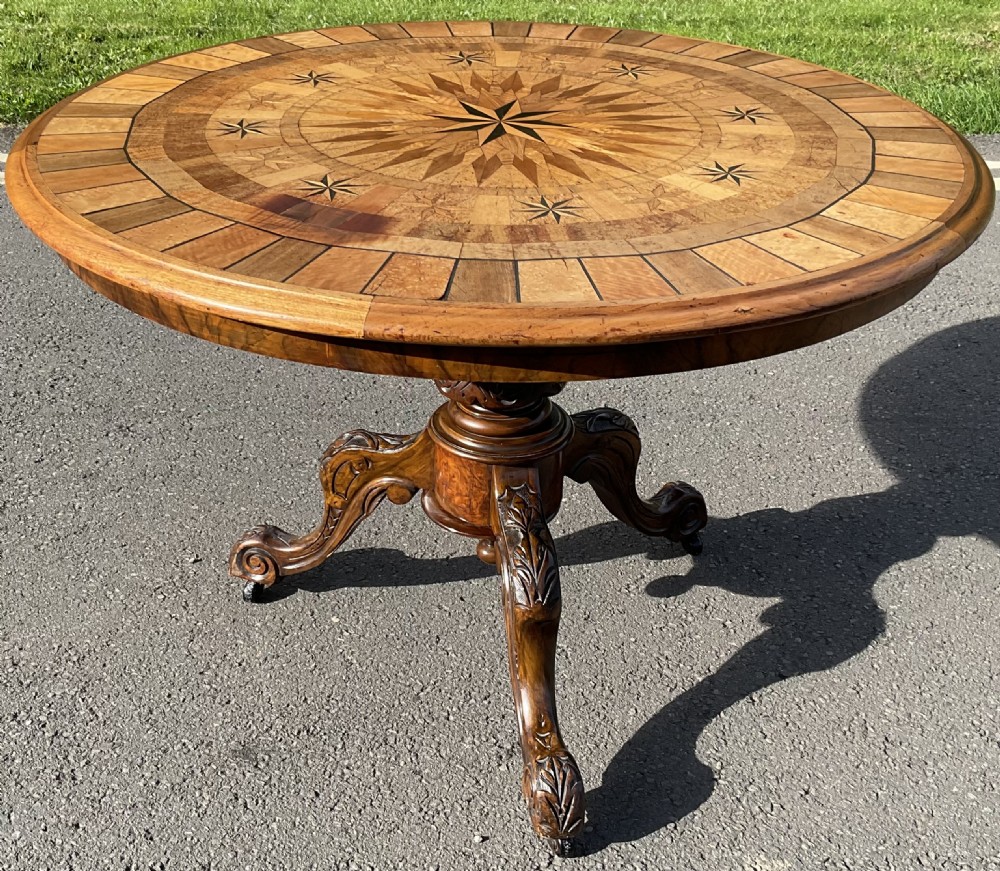 A circular Victorian walnut centre table featuring a complex geometric starburst specimen wood inlay top supported on a carved pedestal base with castors.