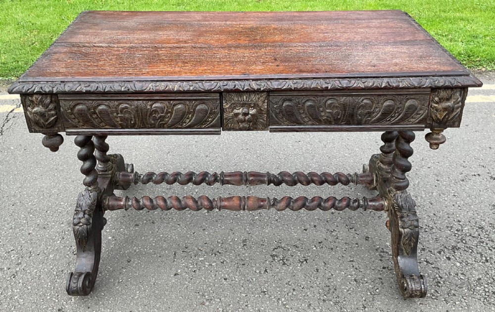 A dark oak writing desk featuring intricate relief carvings, barley twist legs, carved lion mask drawer handles, and double stretchers.
