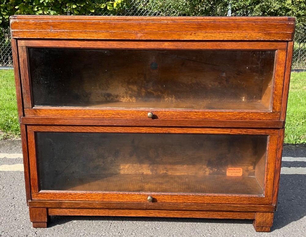 An Edwardian warm brown oak two-tier Globe Wernicke sectional bookcase featuring up-and-over glazed doors with small brass knobs.