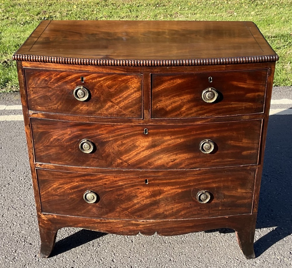 A Georgian flame mahogany bowfront chest of drawers featuring a reeded top edge, two short over two long drawers, brass ring handles, and curved splayed legs.