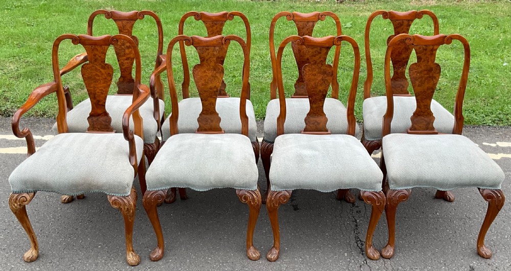 A set of eight Queen Anne style walnut dining chairs featuring figured burr walnut splat backs, carved cabriole legs, and light blue upholstered seats.