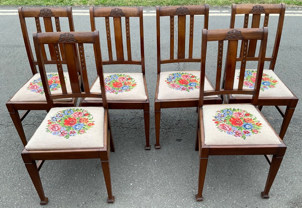 A set of six Edwardian mahogany dining chairs featuring carved crest rails, vertical slat backs, and needlepoint floral seats.