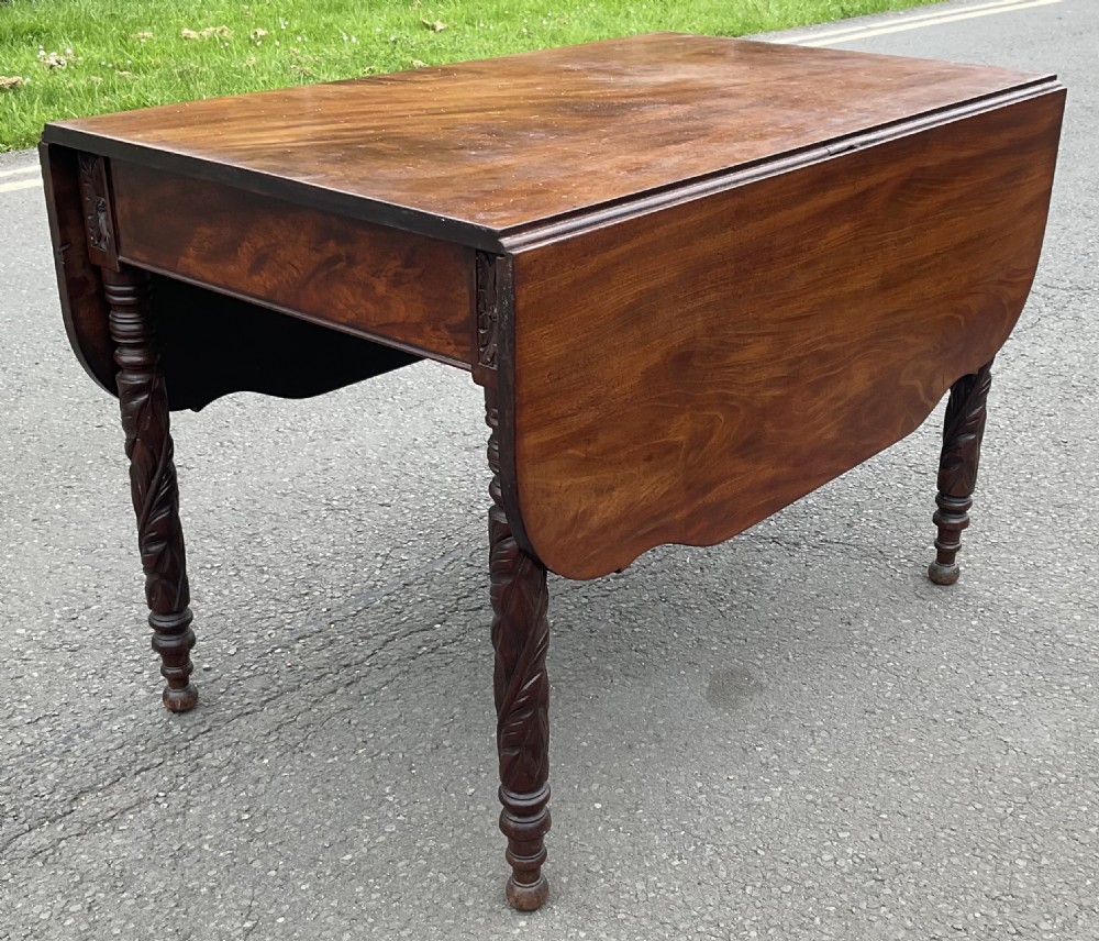 A Regency mahogany Pembroke table featuring two drop-down side flaps and four spiral-turned legs resting on a paved surface.