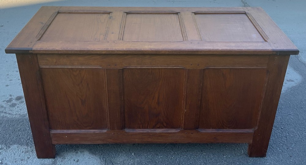 A rectangular solid oak blanket chest featuring three inset panels on the top hinged lid and front face, with visible wooden peg joinery.