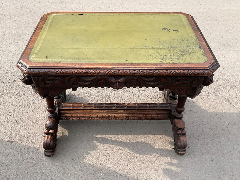 A Victorian carved oak centre table featuring a green leather inset top, detailed scroll and mask frieze carvings, and robust turned supports with a carved stretcher.