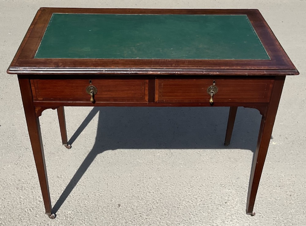 An Edwardian inlaid mahogany writing desk featuring a green leather top insert, two frieze drawers with brass handles, and square tapered legs on castors.