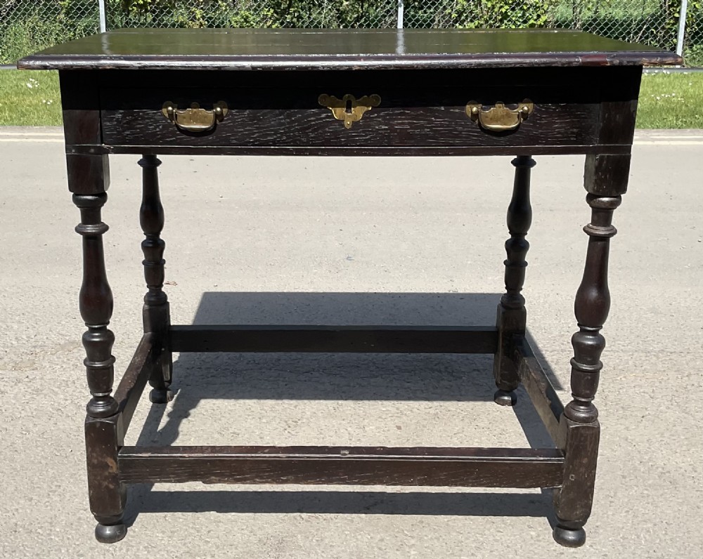 A Georgian dark oak side table with turned legs, lower stretchers, and a single drawer featuring brass handles.