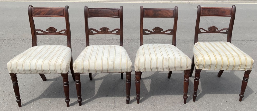 A set of four Georgian mahogany dining chairs featuring carved back rails, turned front legs, and cream striped fabric seats.