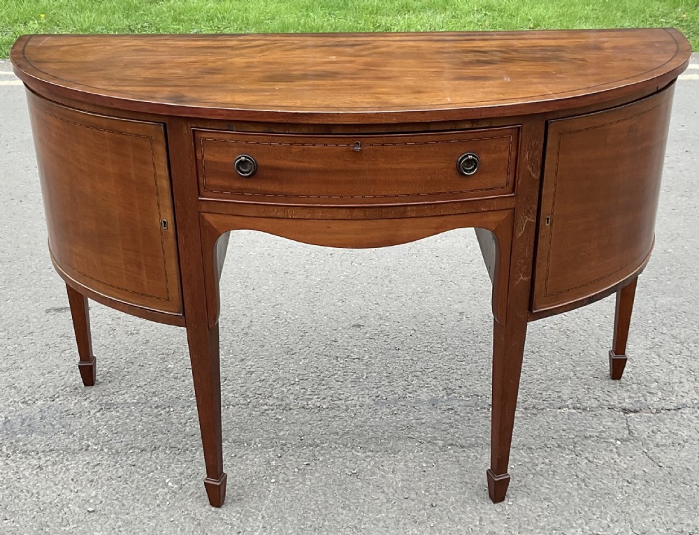 A Georgian mahogany bowfront sideboard with boxwood stringing, a central drawer, two side cupboards, and square tapered legs terminating in spade feet.