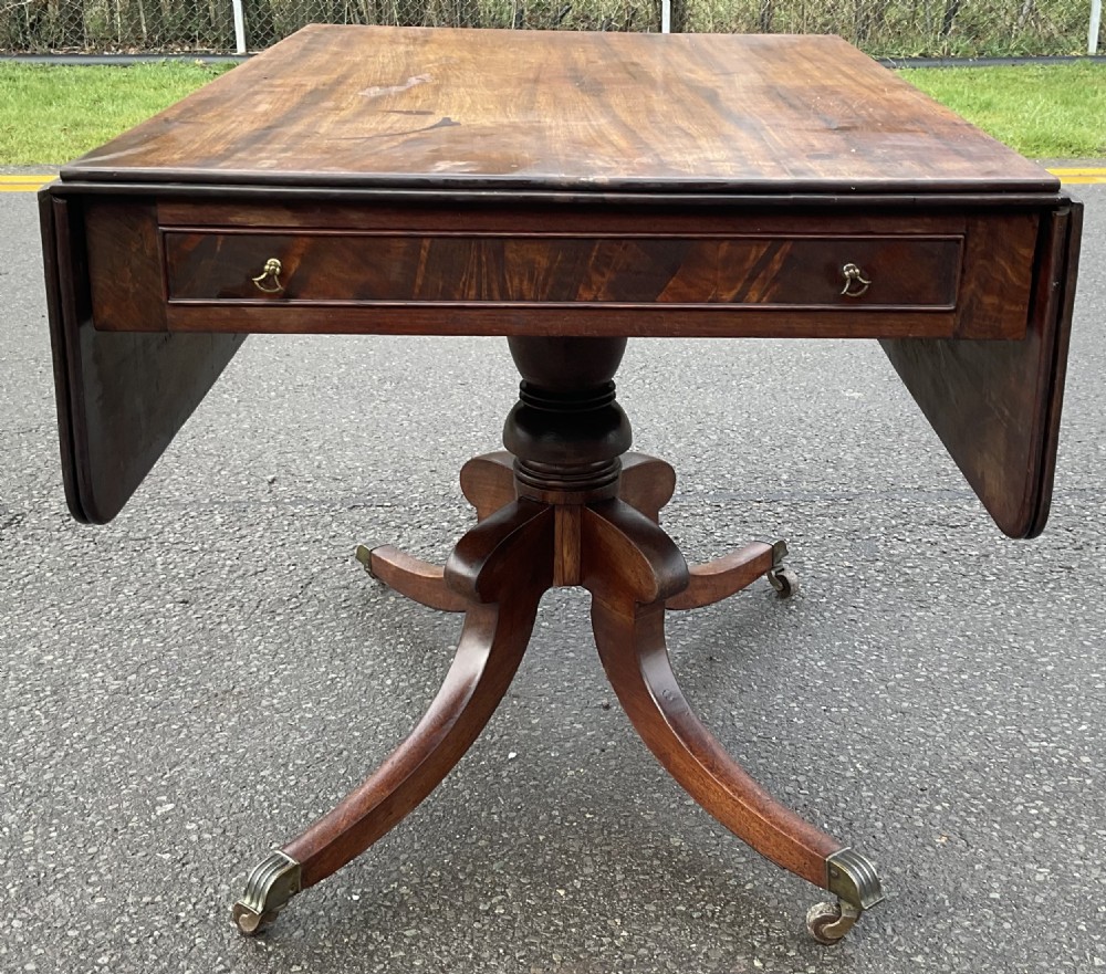 A Georgian mahogany drop-leaf table featuring a rectangular top, a frieze drawer with brass handles, and a four-legged pedestal base with brass castors. View II