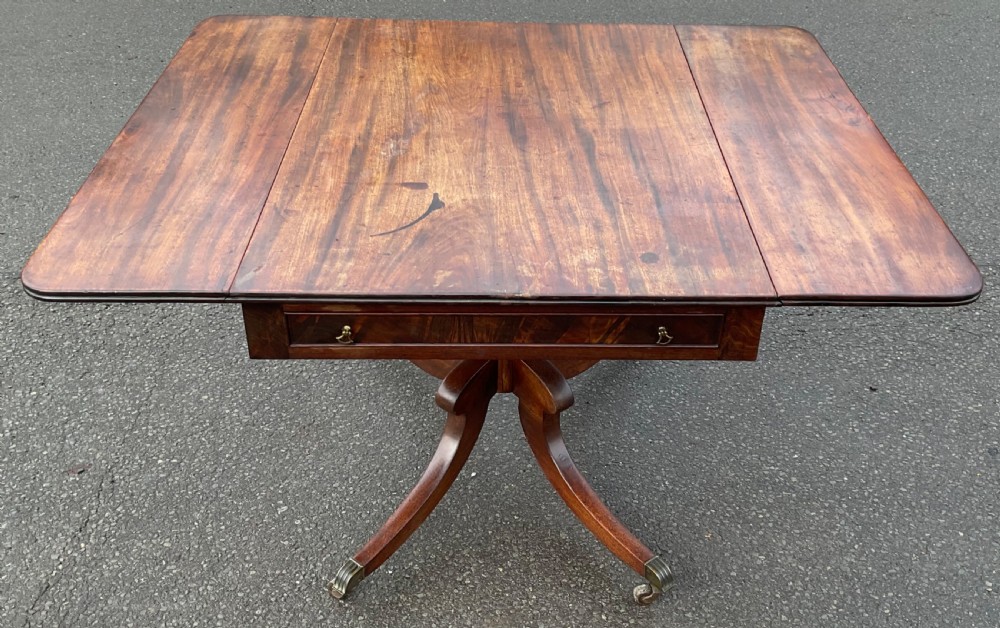 A Georgian mahogany drop-leaf table featuring a rectangular top, a frieze drawer with brass handles, and a four-legged pedestal base with brass castors. View IV