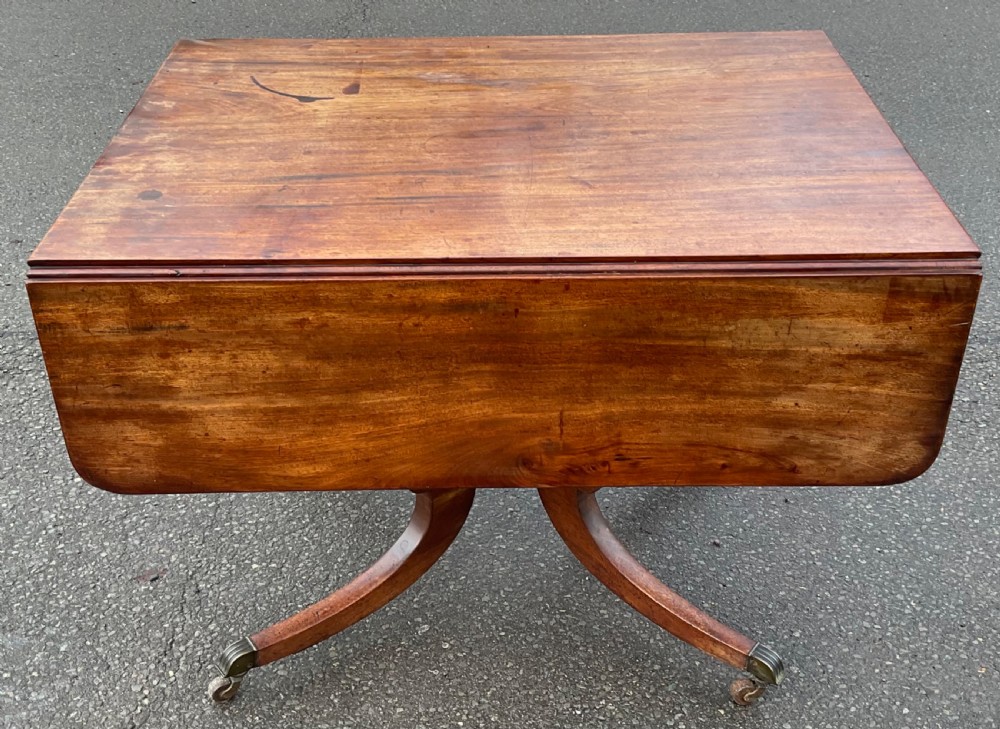 A Georgian mahogany drop-leaf table featuring a rectangular top, a frieze drawer with brass handles, and a four-legged pedestal base with brass castors. View VI