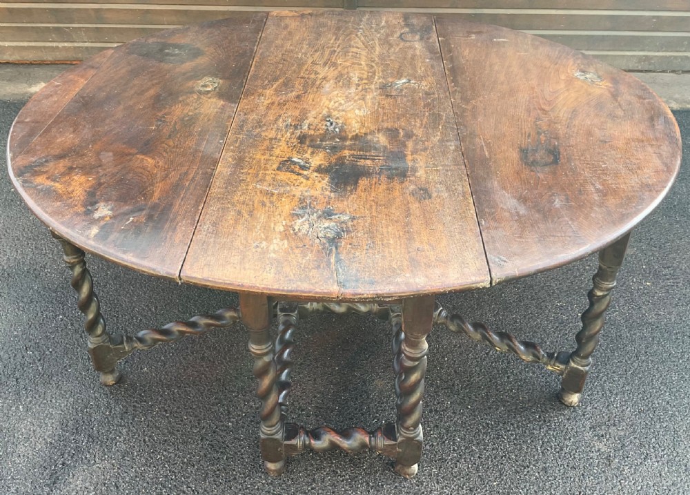 A large antique dark oak gateleg dining table shown extended with round drop leaves and barley twist turned legs.