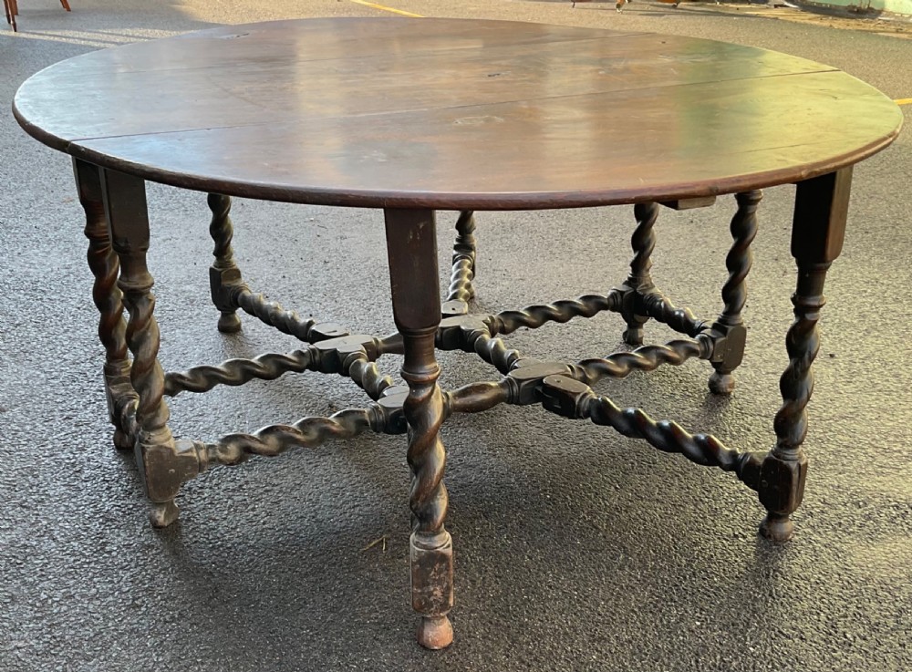 A large antique dark oak gateleg dining table shown extended with round drop leaves and barley twist turned legs. View II