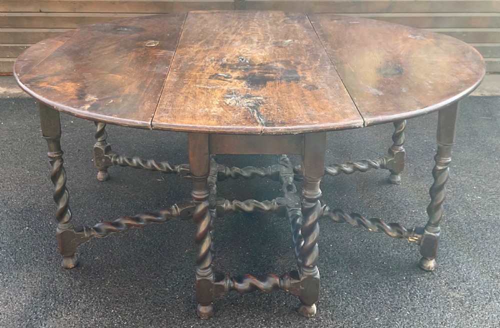 A large antique dark oak gateleg dining table shown extended with round drop leaves and barley twist turned legs. View III
