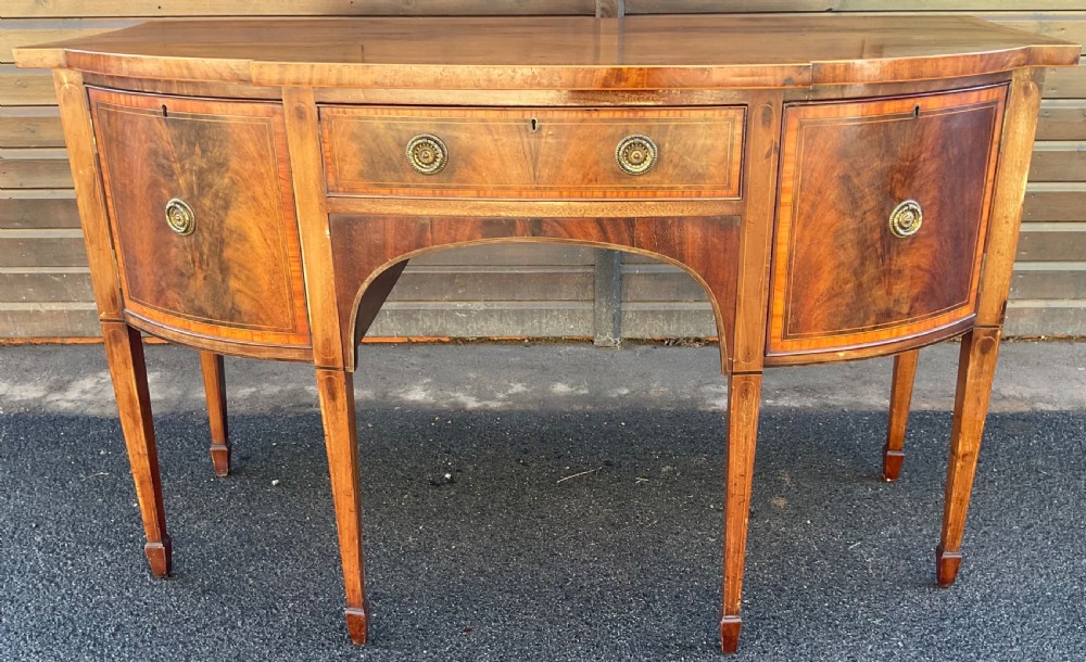 A Georgian mahogany bowfront sideboard featuring six tapered legs, decorative boxwood inlay, and central drawer above an arched apron.
