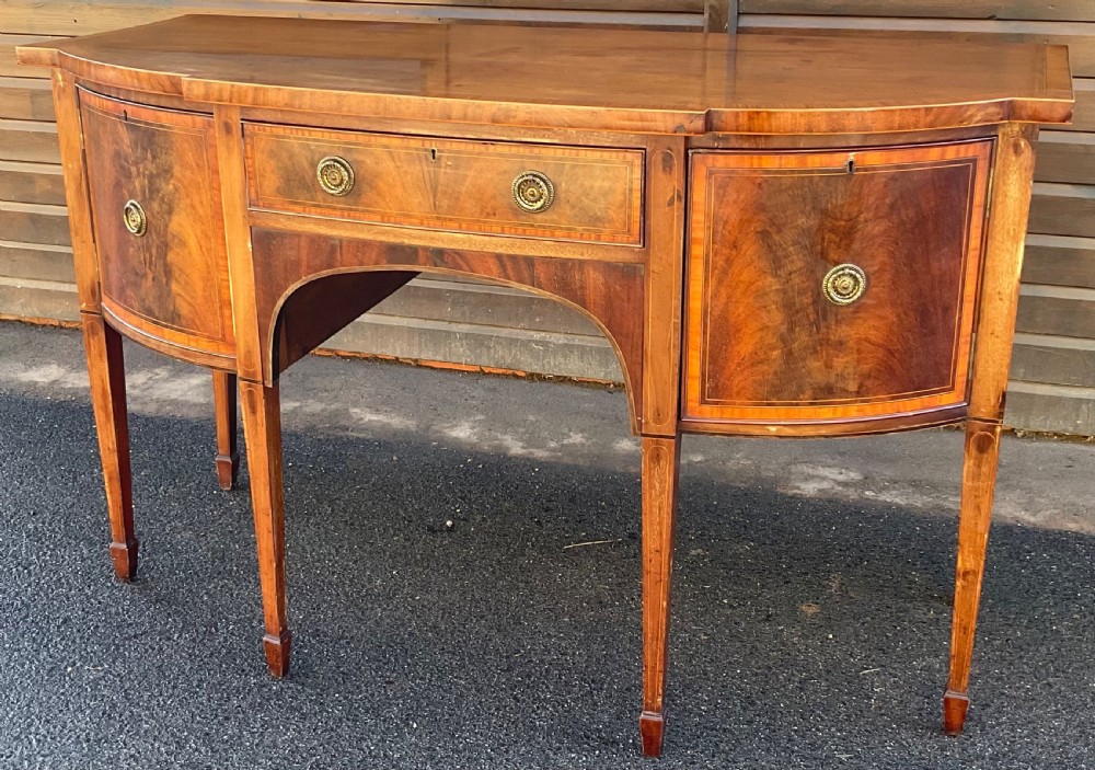 A Georgian mahogany bowfront sideboard featuring six tapered legs, decorative boxwood inlay, and central drawer above an arched apron. View II