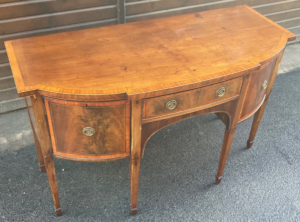 A Georgian mahogany bowfront sideboard featuring six tapered legs, decorative boxwood inlay, and central drawer above an arched apron. View III