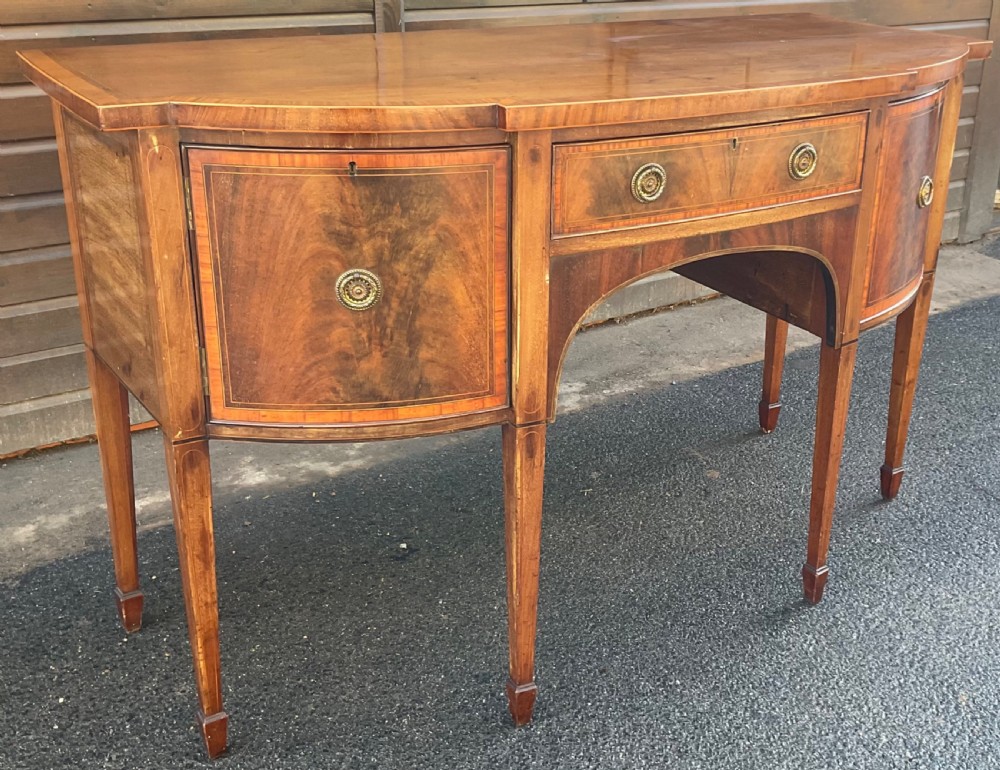 A Georgian mahogany bowfront sideboard featuring six tapered legs, decorative boxwood inlay, and central drawer above an arched apron. View IV