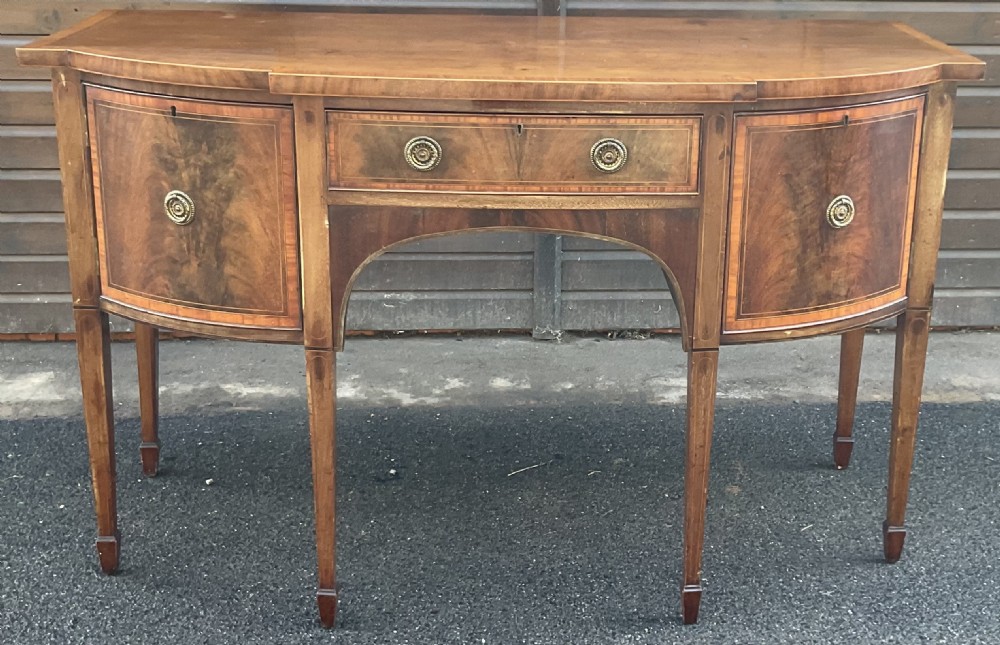 A Georgian mahogany bowfront sideboard featuring six tapered legs, decorative boxwood inlay, and central drawer above an arched apron. View V