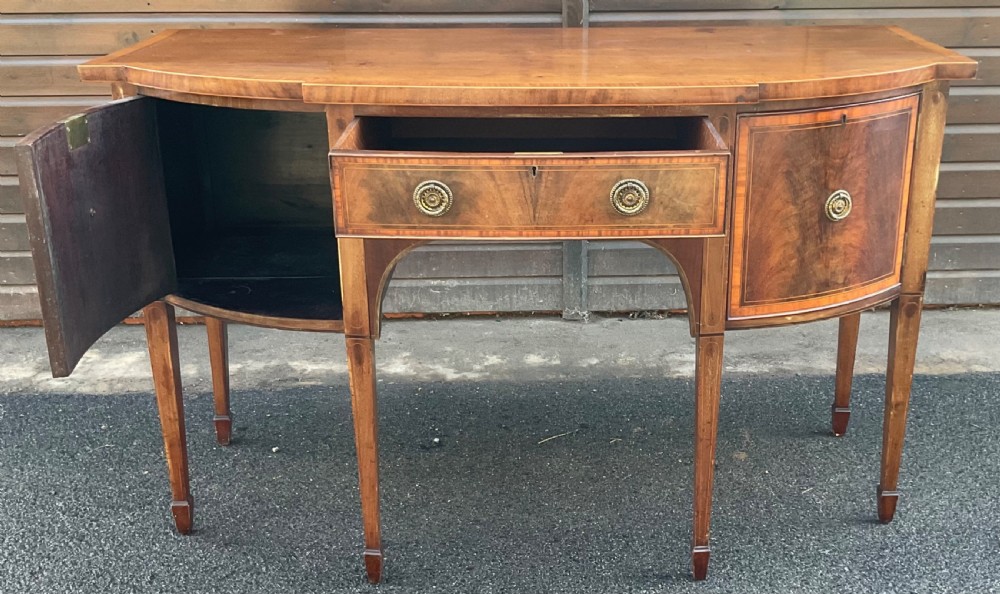 A Georgian mahogany bowfront sideboard featuring six tapered legs, decorative boxwood inlay, and central drawer above an arched apron. View VI