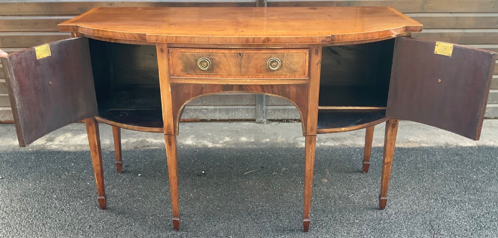 A Georgian mahogany bowfront sideboard featuring six tapered legs, decorative boxwood inlay, and central drawer above an arched apron. View VII