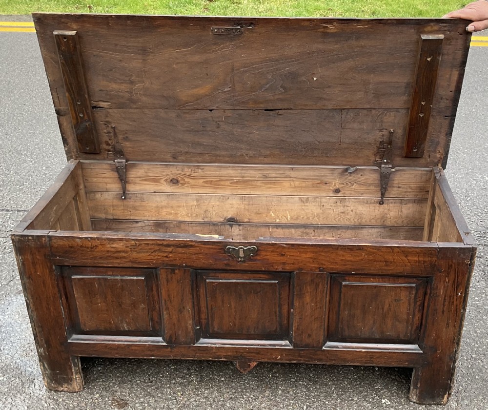 A dark oak antique blanket chest featuring three recessed front panels, a flat top hinged lid, and an iron escutcheon. View VI