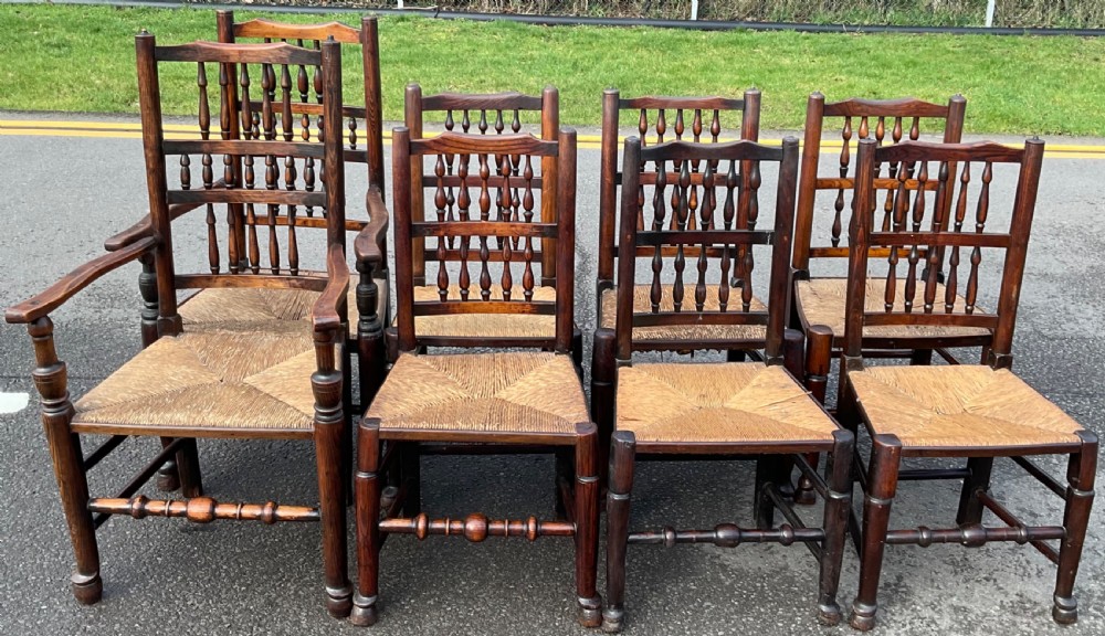 A set of eight Victorian dark elm dining chairs featuring turned spindle backs, side armrests on carvers, and woven rush seats.