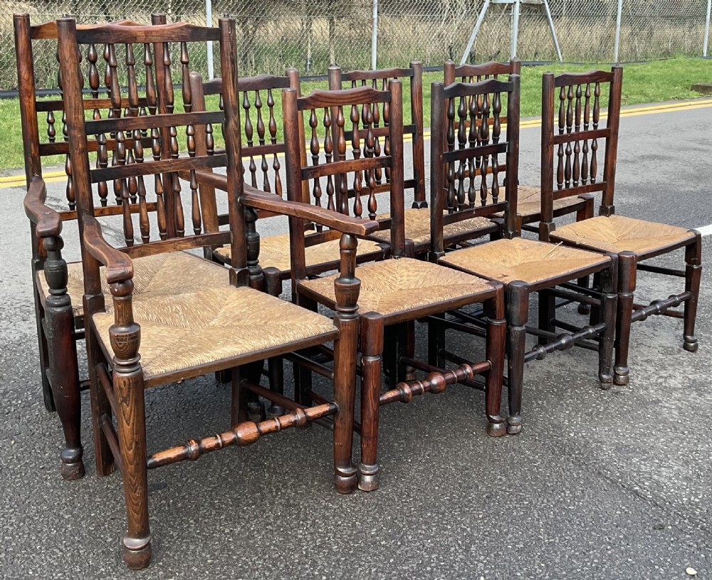 A set of eight Victorian dark elm dining chairs featuring turned spindle backs, side armrests on carvers, and woven rush seats. View II
