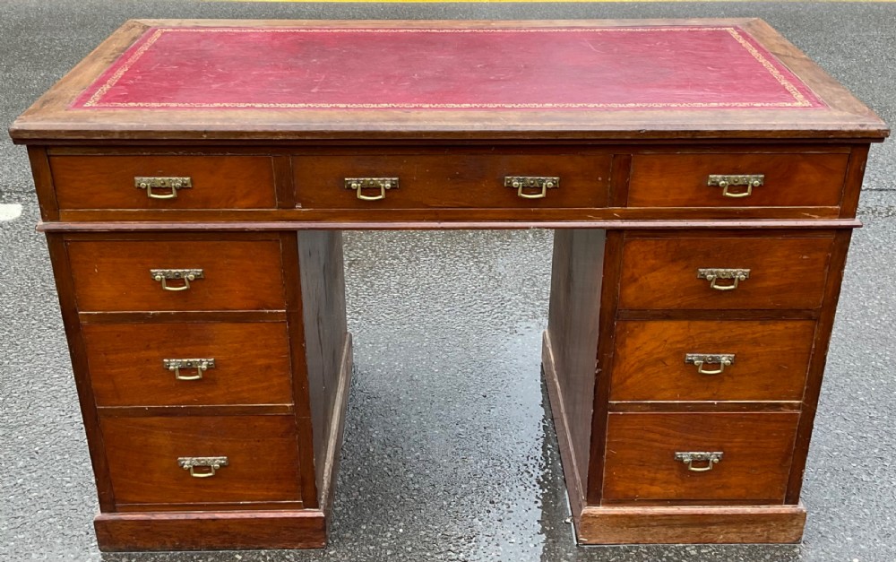 A Victorian mahogany kneehole writing desk featuring a red leather top with gilt tooling and nine brass-handled drawers.