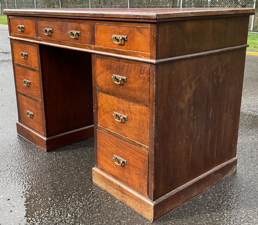 A Victorian mahogany kneehole writing desk featuring a red leather top with gilt tooling and nine brass-handled drawers. View IV