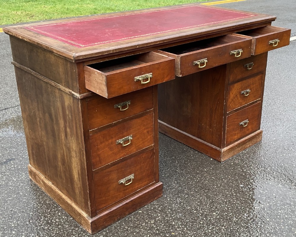 A Victorian mahogany kneehole writing desk featuring a red leather top with gilt tooling and nine brass-handled drawers. View VI