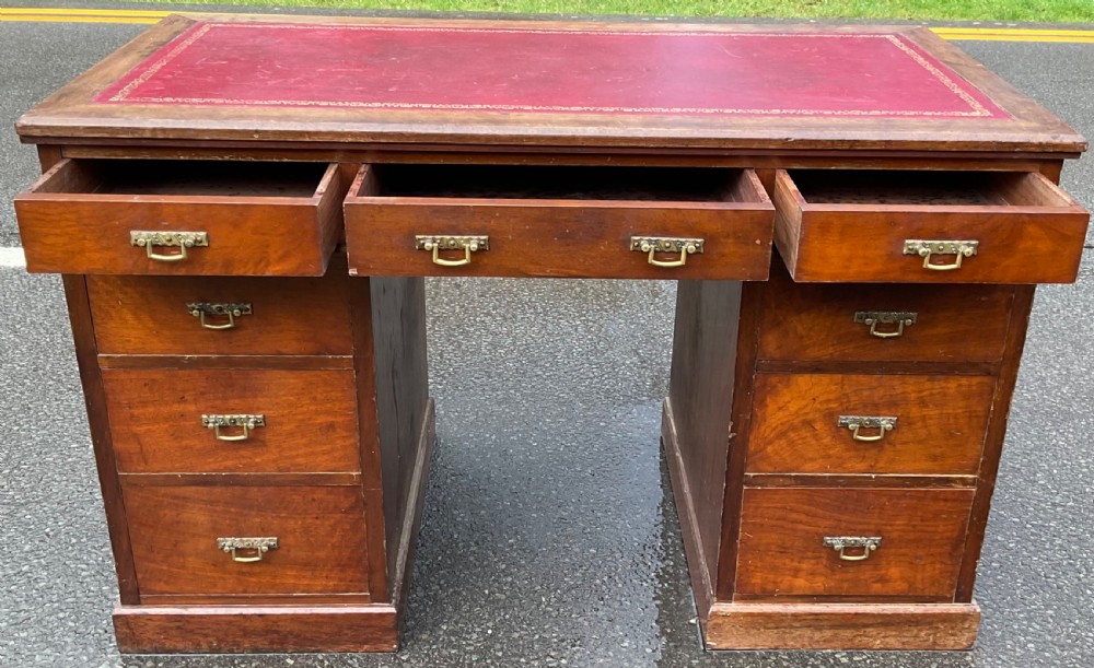 A Victorian mahogany kneehole writing desk featuring a red leather top with gilt tooling and nine brass-handled drawers. View VIII