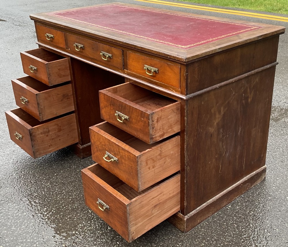 A Victorian mahogany kneehole writing desk featuring a red leather top with gilt tooling and nine brass-handled drawers. View IX