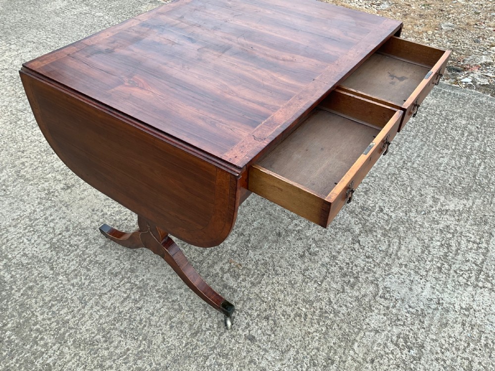 A Regency mahogany sofa table featuring two frieze drawers, drop-leaf ends, decorative string inlay, and splayed legs terminating in brass castors. View II