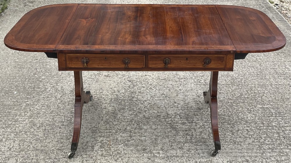 A Regency mahogany sofa table featuring two frieze drawers, drop-leaf ends, decorative string inlay, and splayed legs terminating in brass castors. View IV
