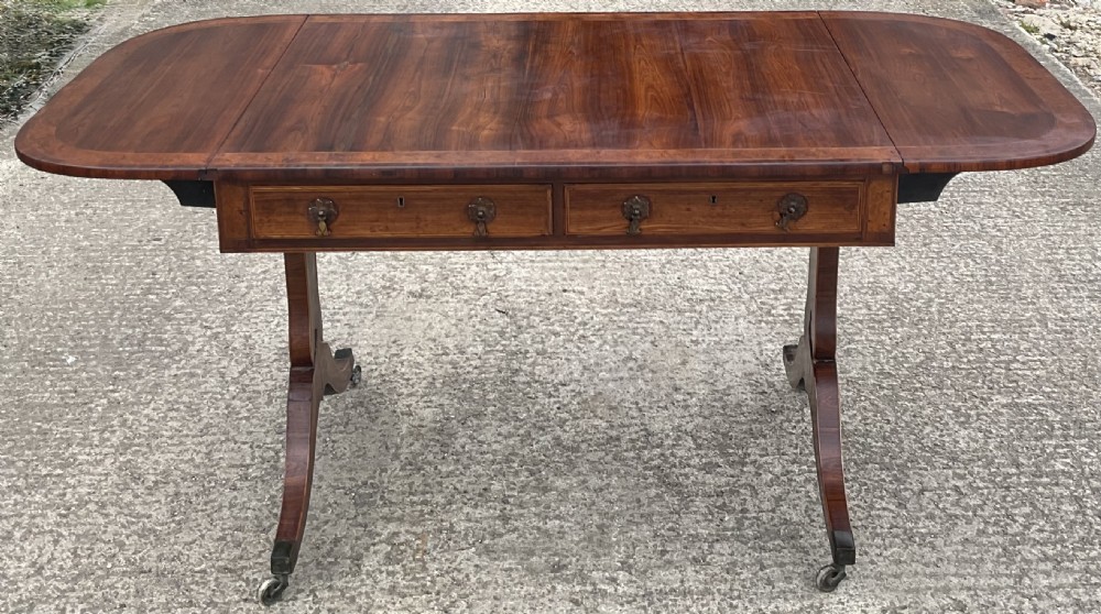 A Regency mahogany sofa table featuring two frieze drawers, drop-leaf ends, decorative string inlay, and splayed legs terminating in brass castors. View VI