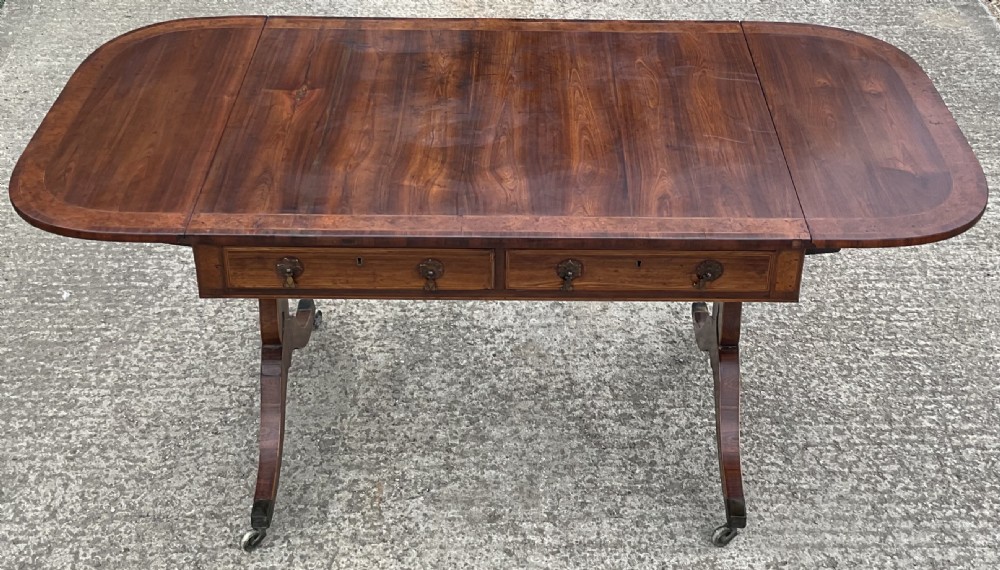 A Regency mahogany sofa table featuring two frieze drawers, drop-leaf ends, decorative string inlay, and splayed legs terminating in brass castors. View VII