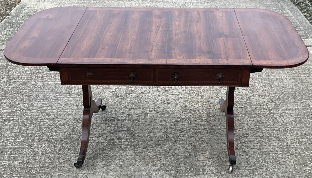 A Regency mahogany sofa table featuring two frieze drawers, drop-leaf ends, decorative string inlay, and splayed legs terminating in brass castors. View VIII