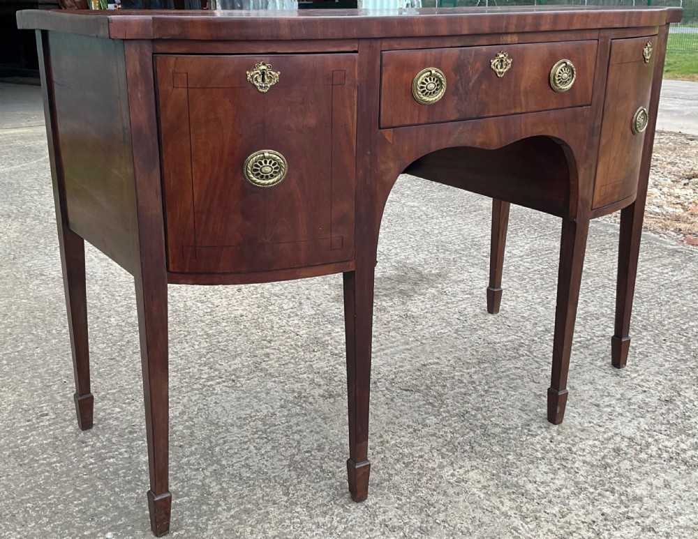 A Georgian mahogany bowfront sideboard featuring a central drawer flanked by two side cupboards, brass handles, and square tapered legs with spade feet. View II