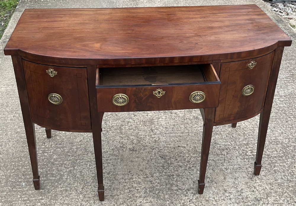 A Georgian mahogany bowfront sideboard featuring a central drawer flanked by two side cupboards, brass handles, and square tapered legs with spade feet. View III