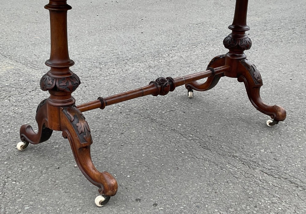 A Victorian burr walnut writing table featuring floral marquetry inlays, two frieze drawers, carved leg supports, a turned stretcher, and brass castors. View VIII